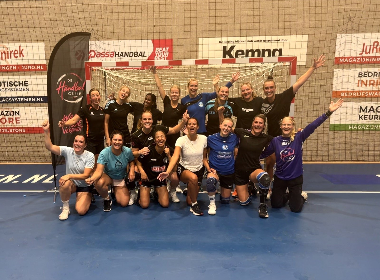 Zestien lachende speelsters van de Handbalclub met de armen omhoog voor het doel in de sporthal, na de eerste Skillz & Play Night.